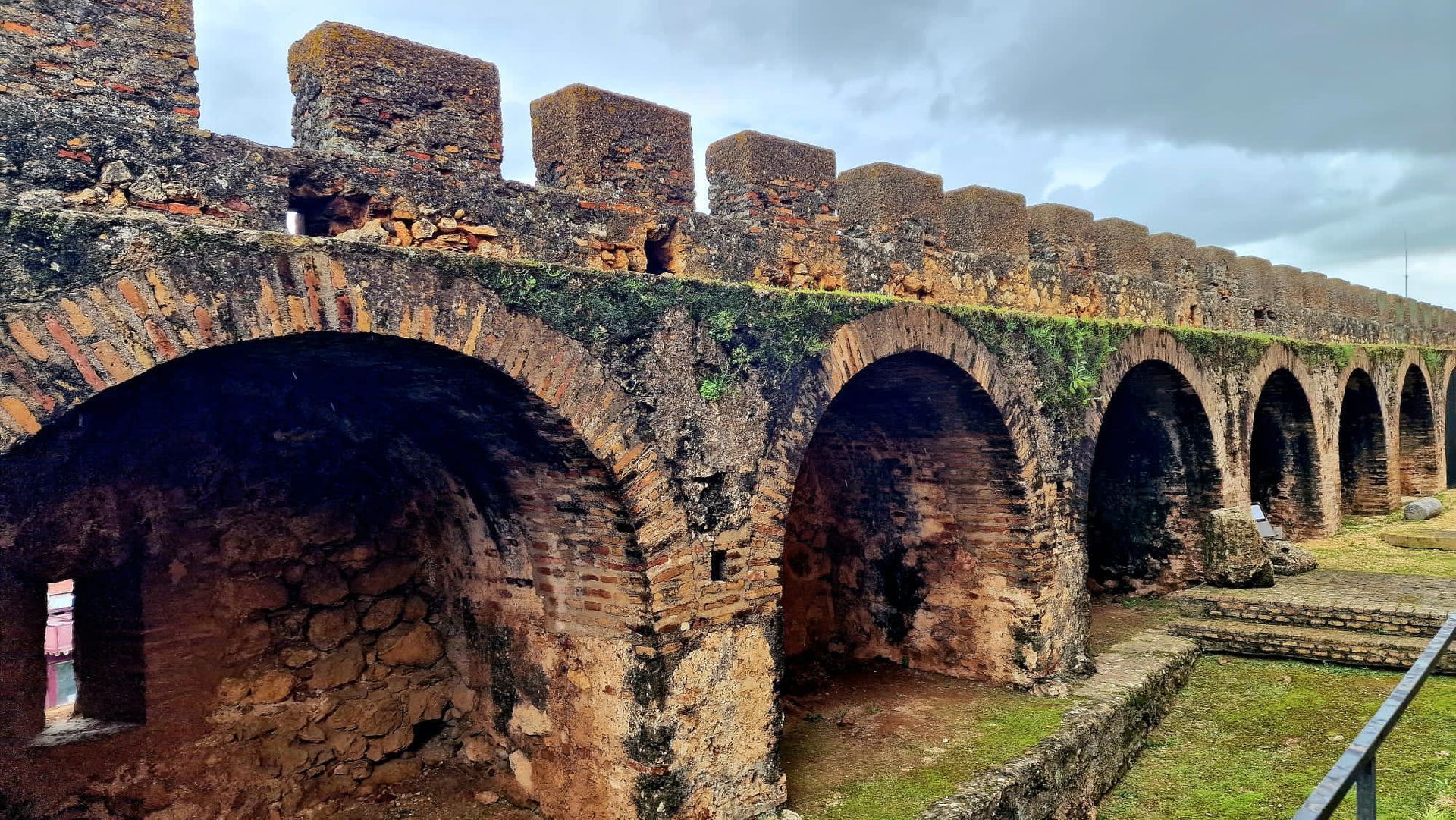 Ruinas de un puente de piedra con varios arcos bajo un cielo nublado, visto de lado