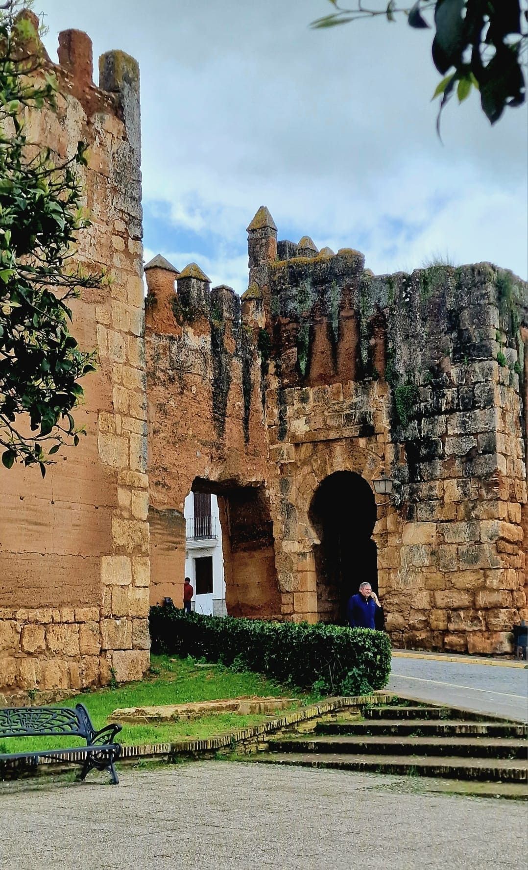Antigua muralla de piedra de una fortaleza con puerta arqueada, escalones y una persona vestida de azul cerca de la entrada