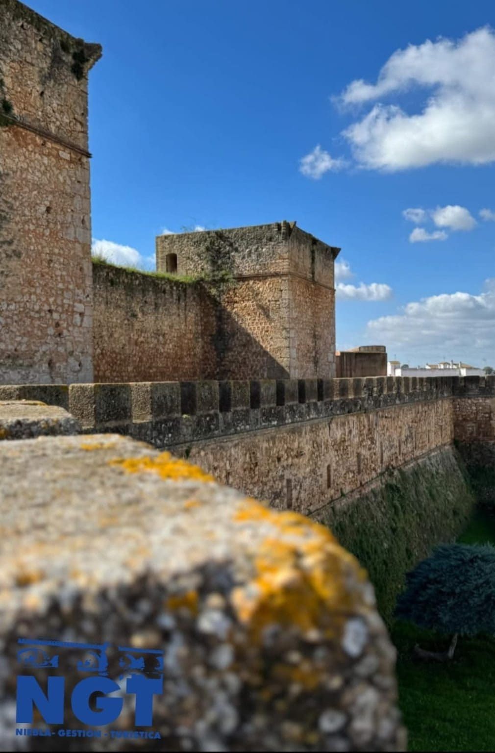 Murallas de piedra de una fortaleza bajo un cielo azul despejado con unas pocas nubes.