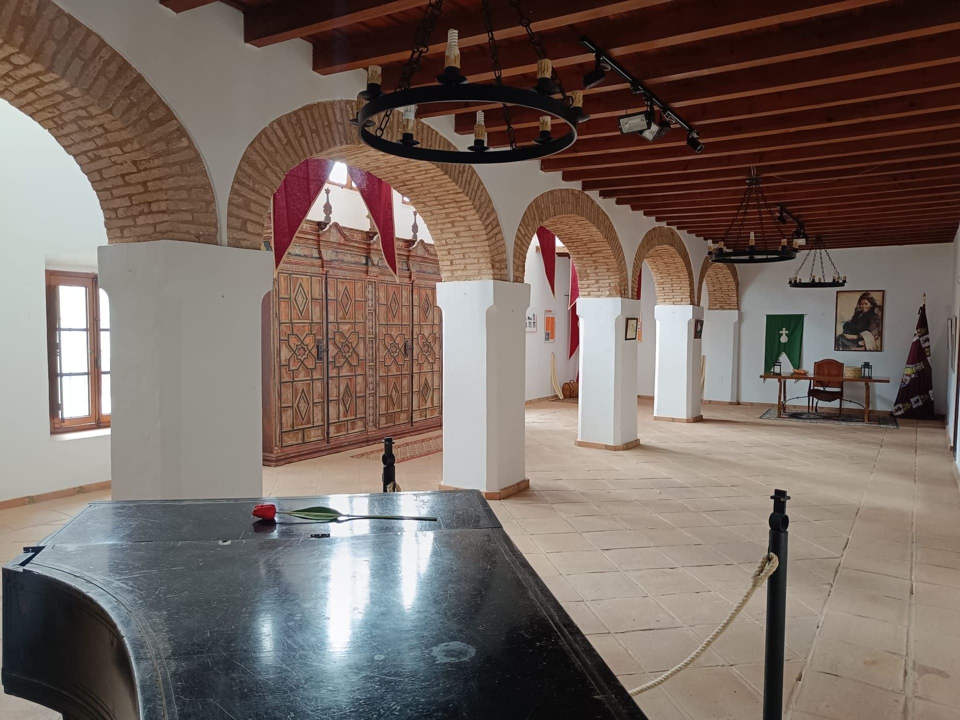Sala de museo histórico con paredes de ladrillo arqueadas, pilares blancos, vigas de madera y una gran mesa negra delante