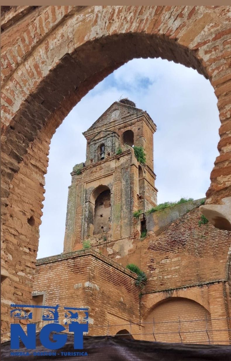 Torre de una antigua iglesia de ladrillo enmarcada por un arco en ruinas bajo un cielo azul
