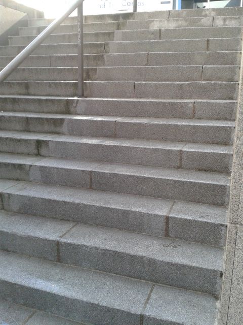 Escaleras de hormigón gris con pasamanos metálico, ascendentes al exterior.