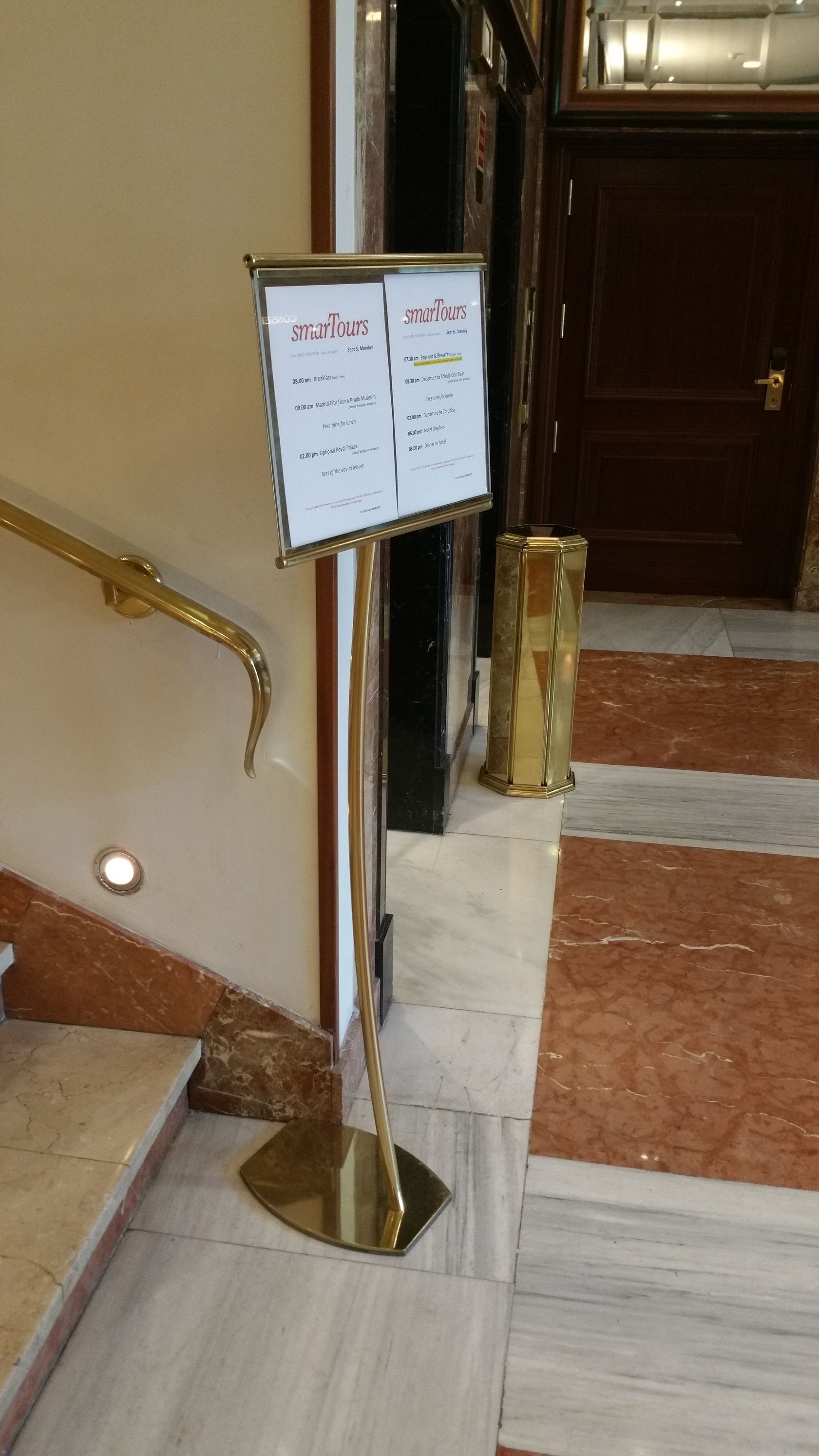 Un expositor de menú dorado sobre unos escalones de mármol cerca de una puerta.