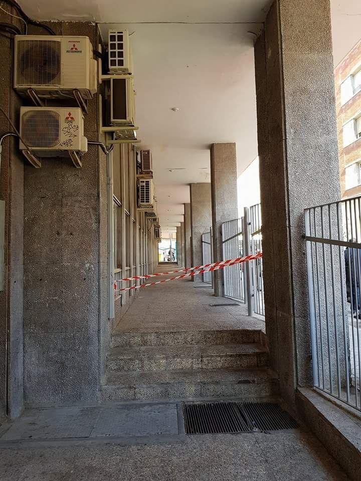 Pasarela exterior revestida con pilares de hormigón, escaleras, cinta de precaución y unidades de aire acondicionado.