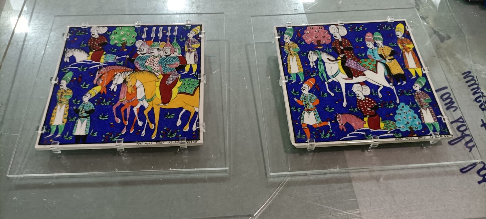 Dos vibrantes piezas de arte en mosaico cuadradas que representan figuras a caballo, exhibidas sobre soportes transparentes.