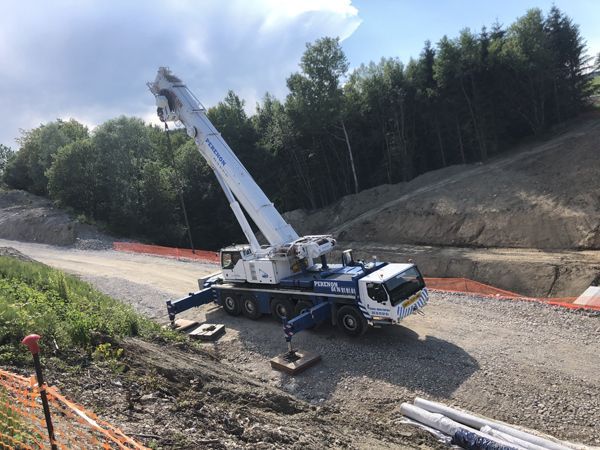 Camion-grue sur un chemin de terre dans une zone de construction boisée, avec des barrières de sécurité orange.