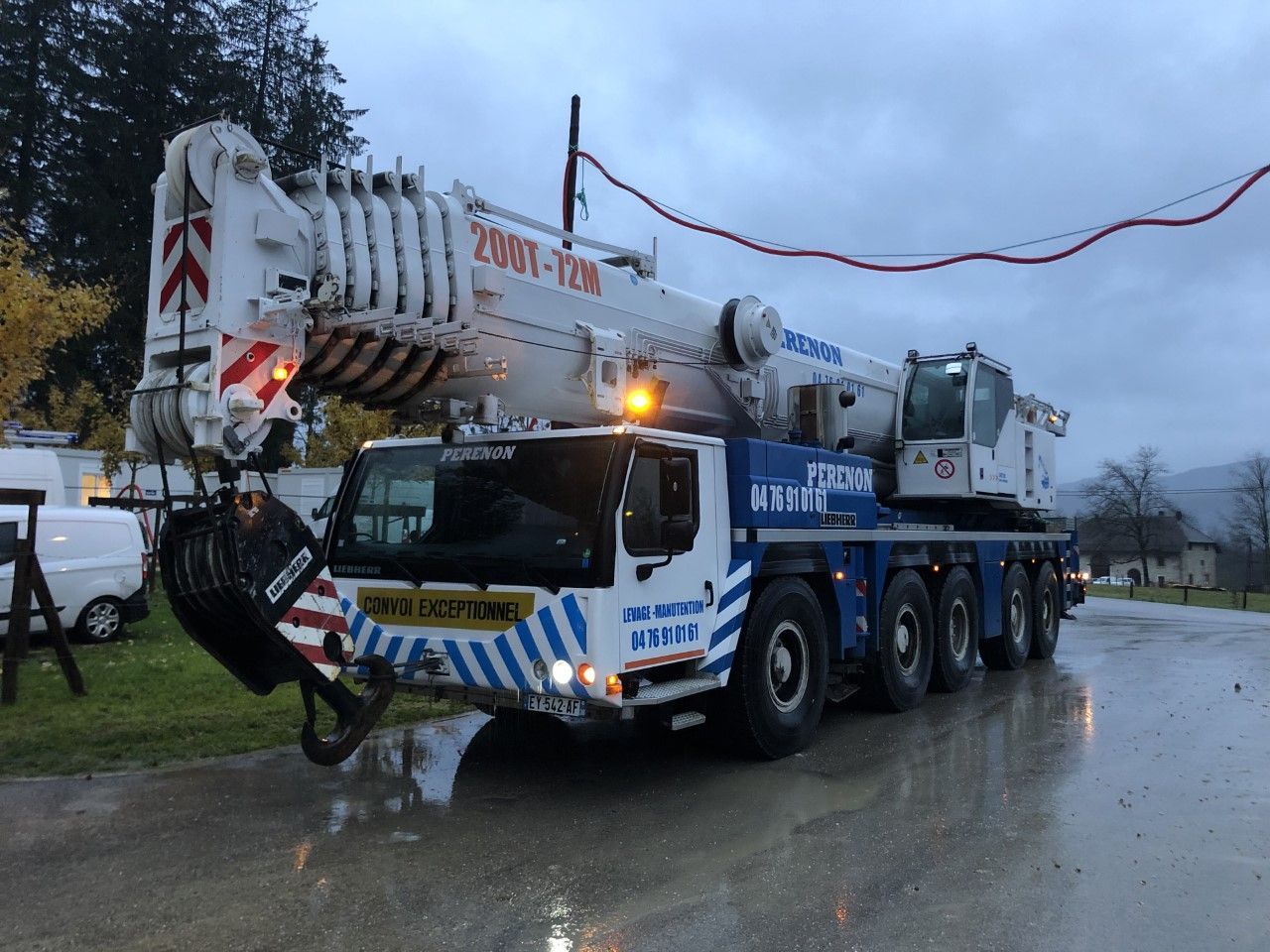 Un gros camion-grue blanc à rayures bleues circule sur une route mouillée par temps pluvieux.