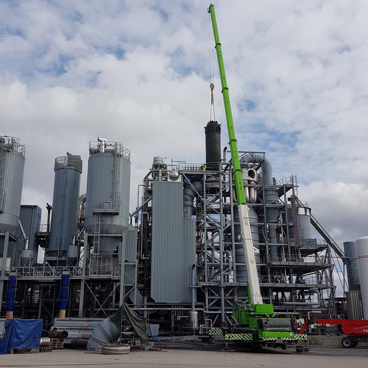 Usine industrielle en construction avec une grue vert vif et de grands silos métalliques sous un ciel nuageux