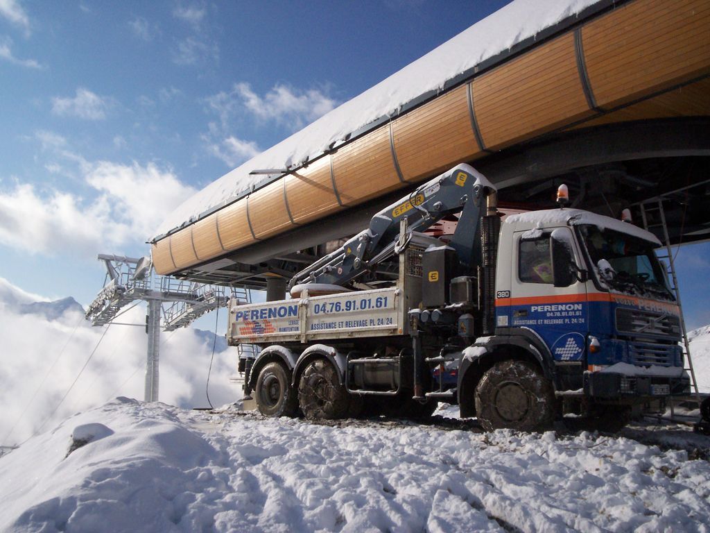 Un camion chasse-neige dégage la neige épaisse à côté d'une structure surélevée dans une zone industrielle enneigée.