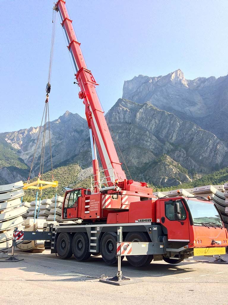 Camion-grue rouge soulevant du matériel sur un chantier de construction en montagne sous un ciel dégagé