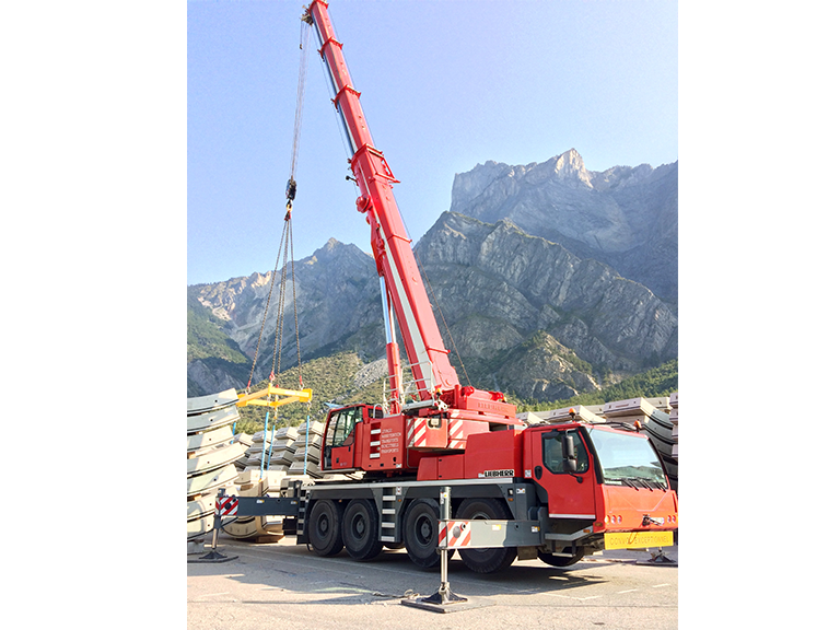 Camion-grue rouge stationné devant des montagnes rocheuses sous un ciel dégagé.