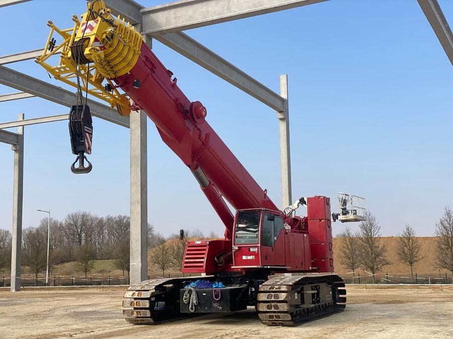 Grue sur chenilles rouge soulevant une poutre d'acier sur un chantier de construction extérieur