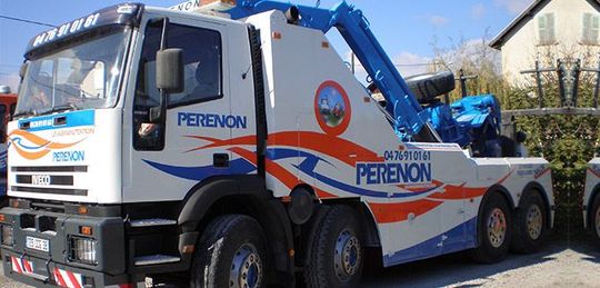 Une dépanneuse blanche et bleue est stationnée dans une rue bordée de maisons.