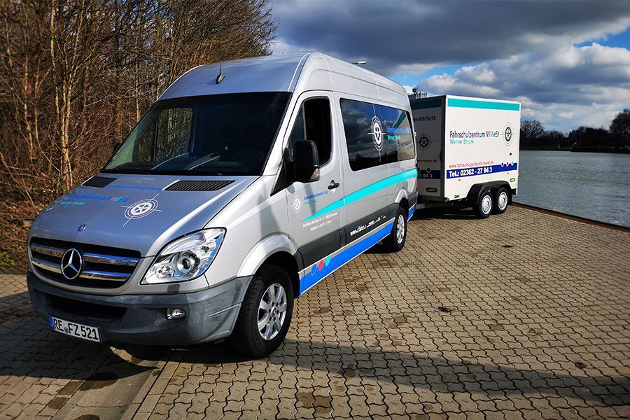 Ein Mercedes Sprinter Van ist auf einem gepflasterten Gehweg neben einem Anhänger geparkt.