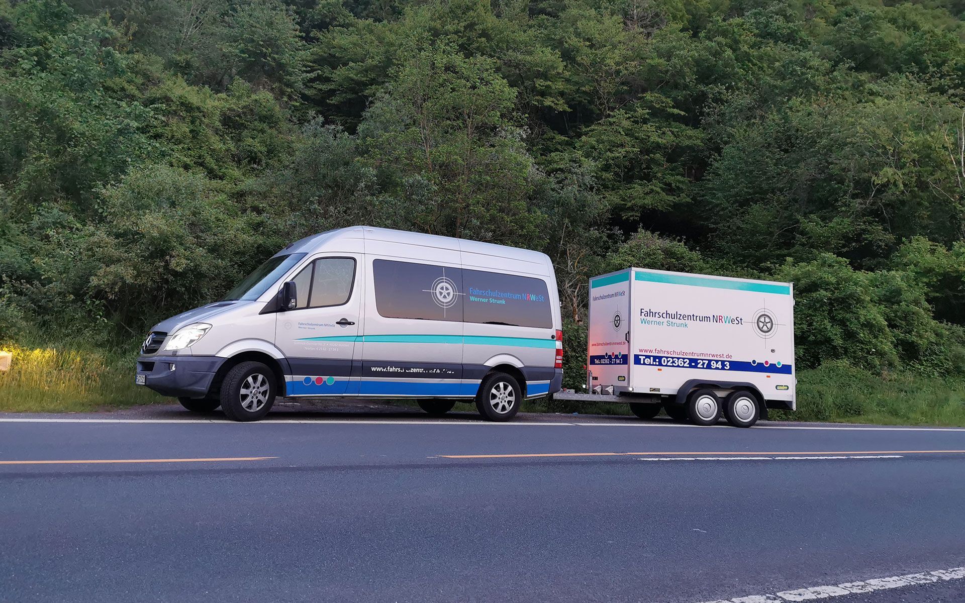 Am Straßenrand parkt ein weißer Lieferwagen mit einem Anhänger.