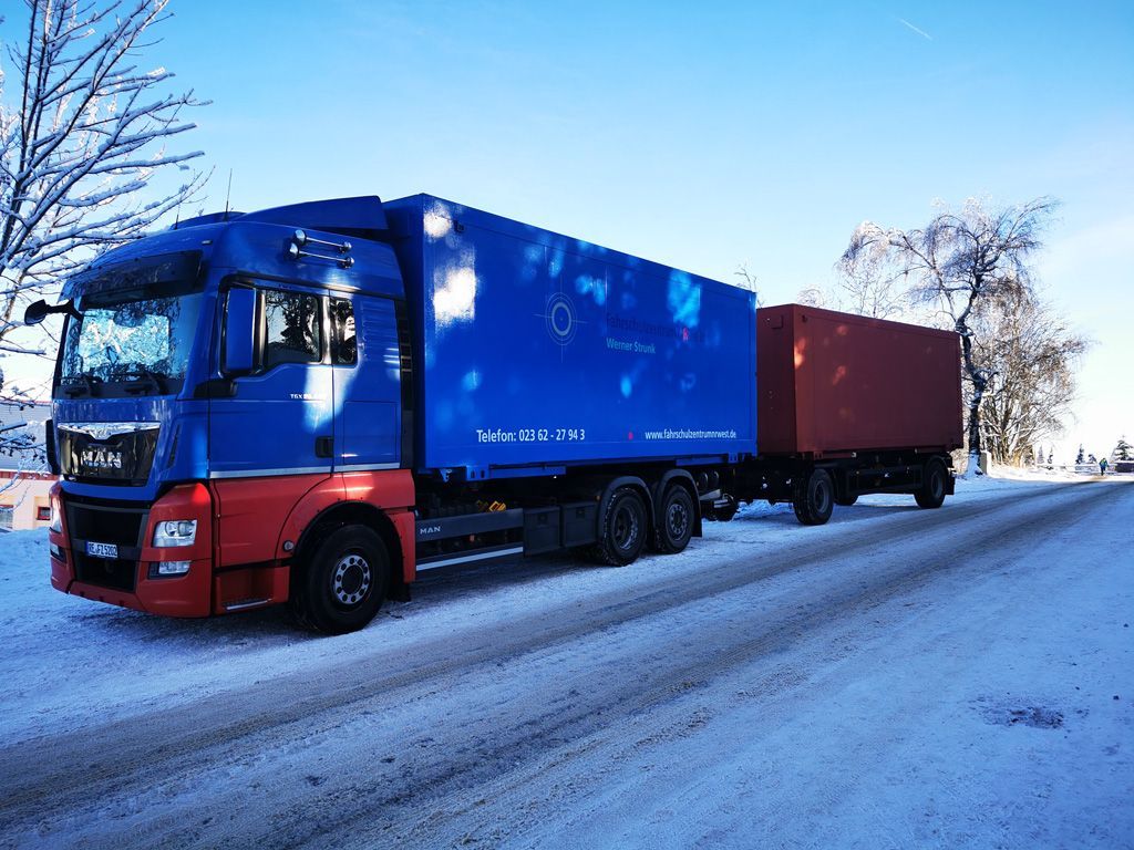 Ein blau-roter Lastwagen parkt auf einer verschneiten Straße.