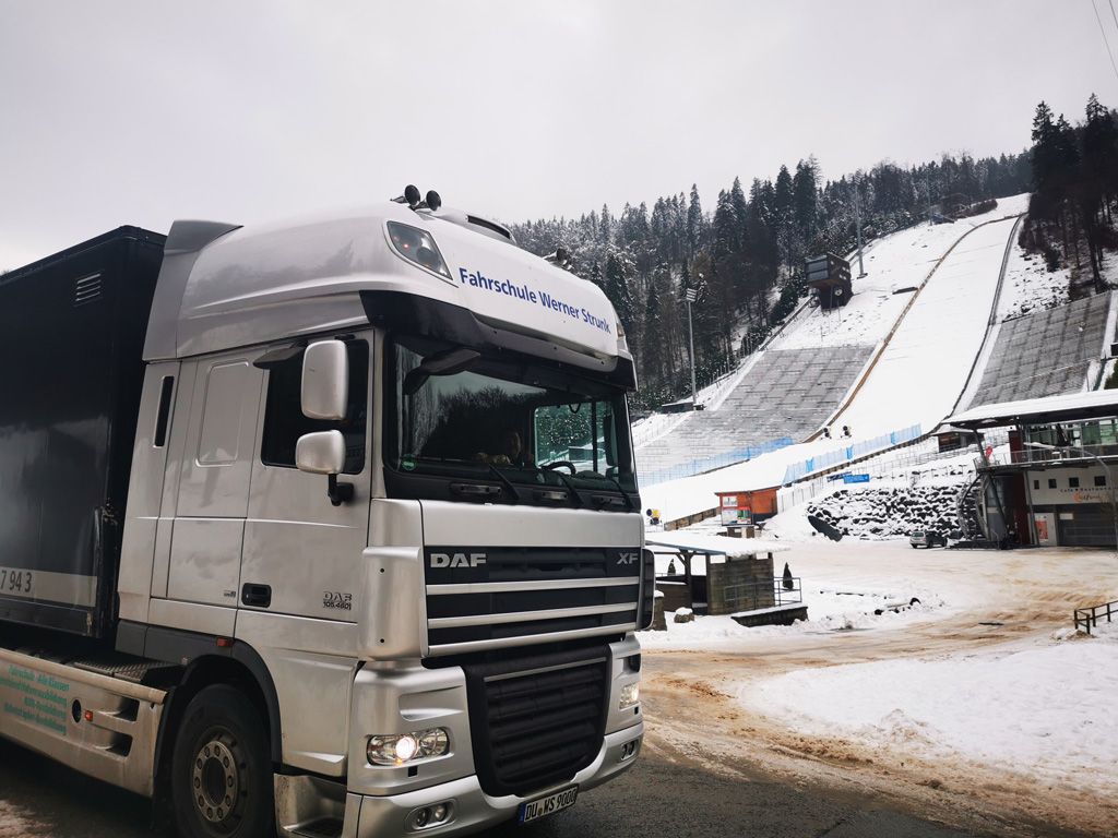 Ein weißer Lastwagen parkt vor einem schneebedeckten Berg.