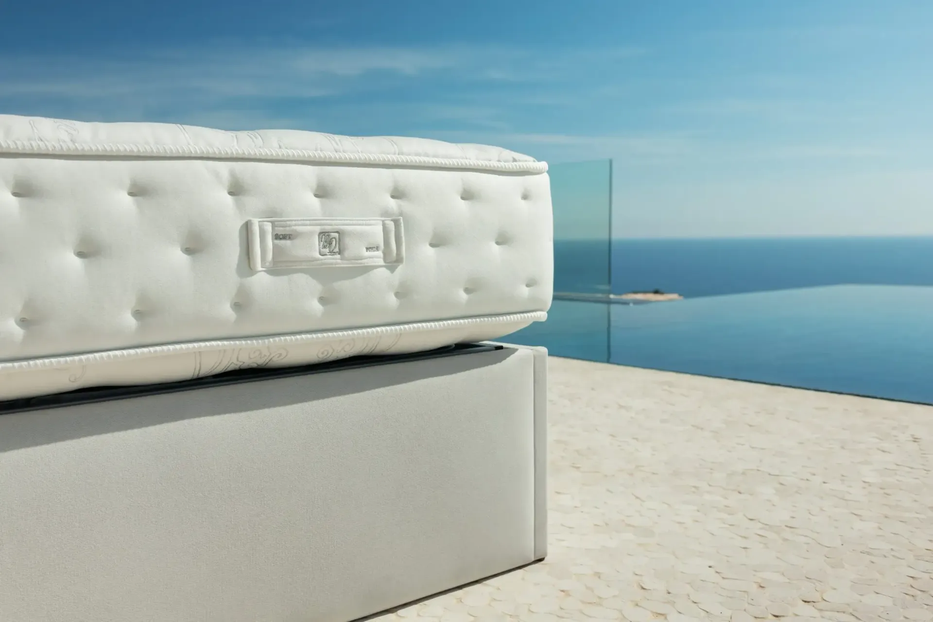Sofá blanco capitoné junto a una barandilla de cristal con vistas a un mar y un cielo azules y tranquilos.