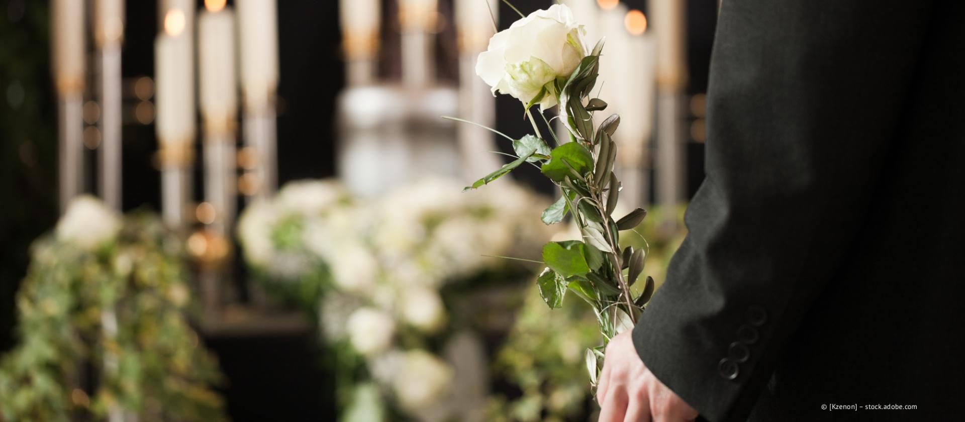 Person mit einer weißen Blume an einem kerzenbeleuchteten Traueraltar