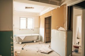 Renovación de baño: bañera con patas, paneles de yeso, escombros de construcción, paredes expuestas.