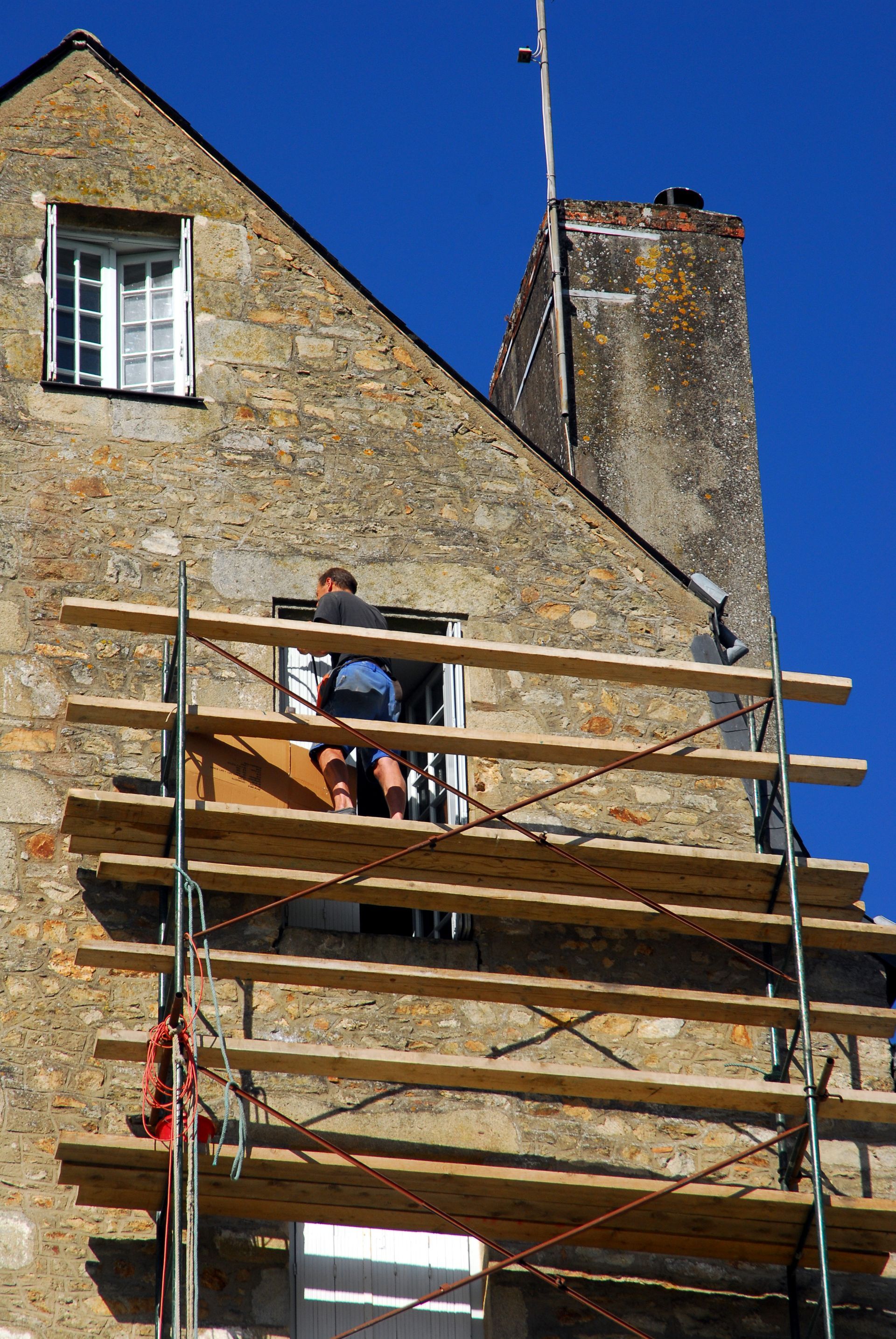 Un ouvrier du bâtiment sur un échafaudage en train de réaliser un ravalement de façade
