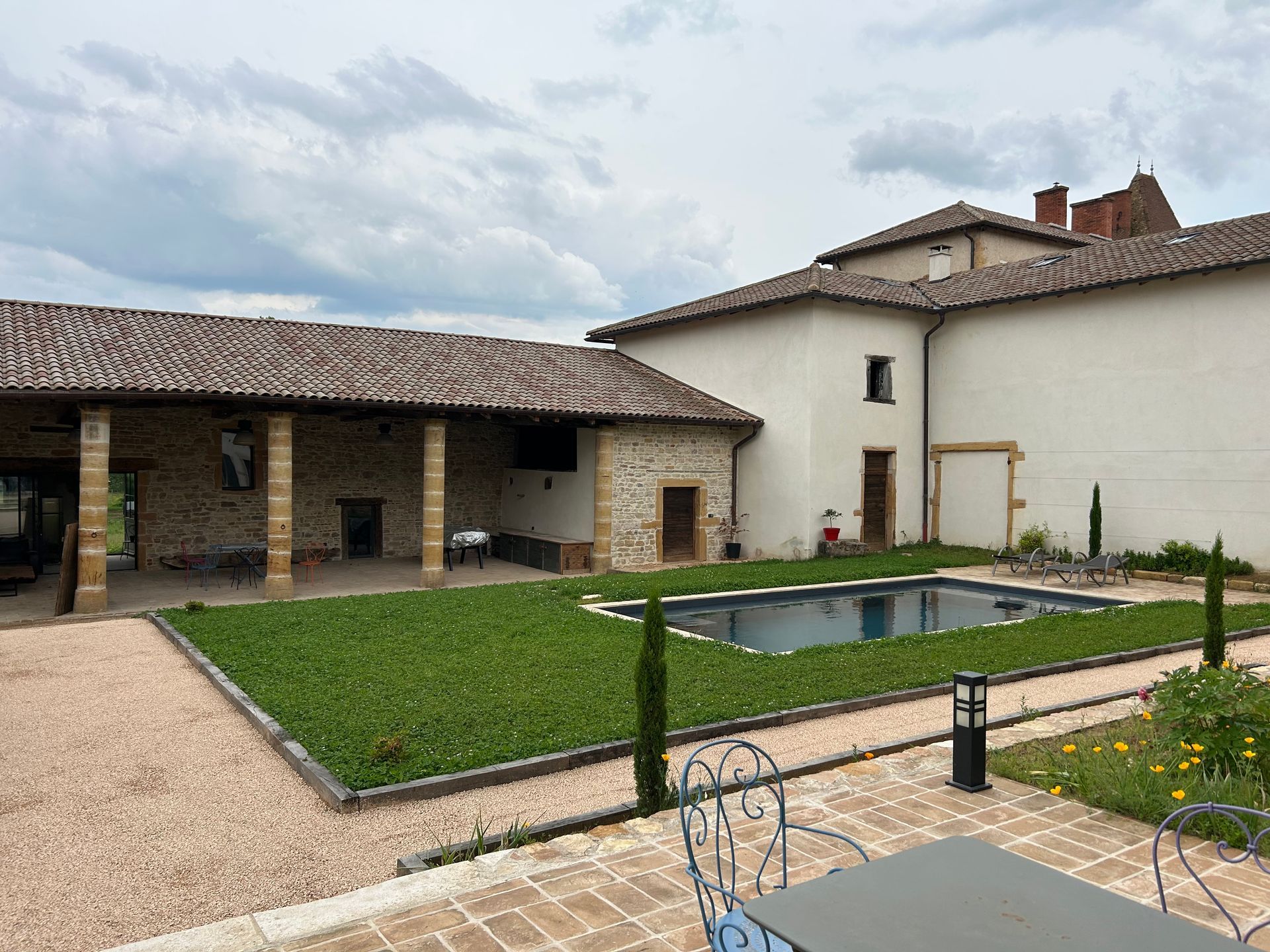 Vue extérieure d'une villa en pierre avec piscine, pelouse et chemin de gravier par temps nuageux.