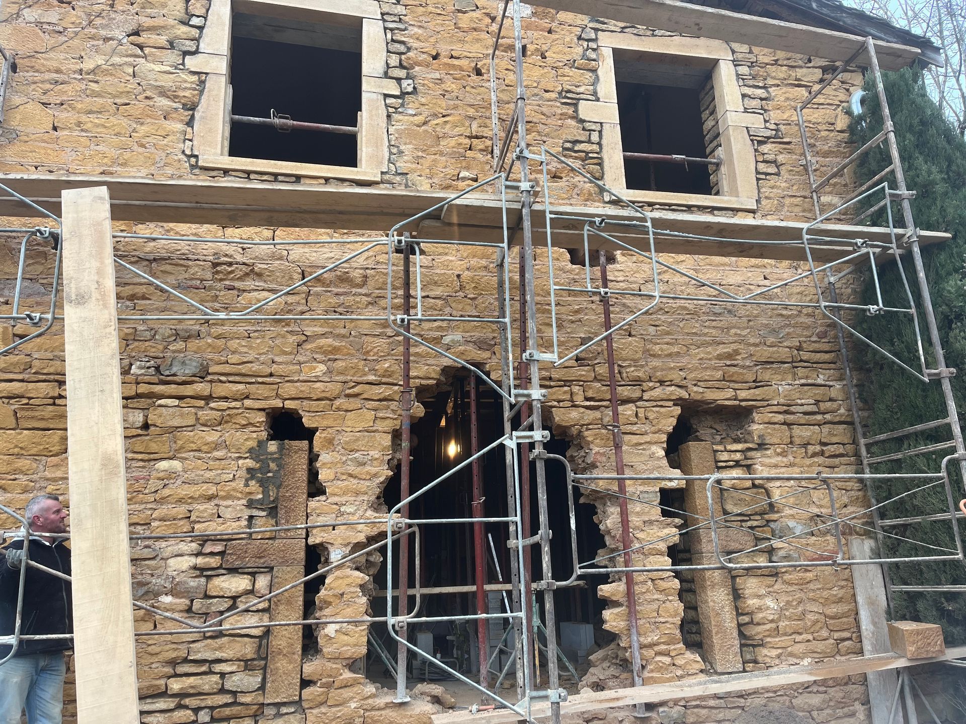 Façade d'immeuble en pierre en cours de rénovation avec échafaudage et grand trou.