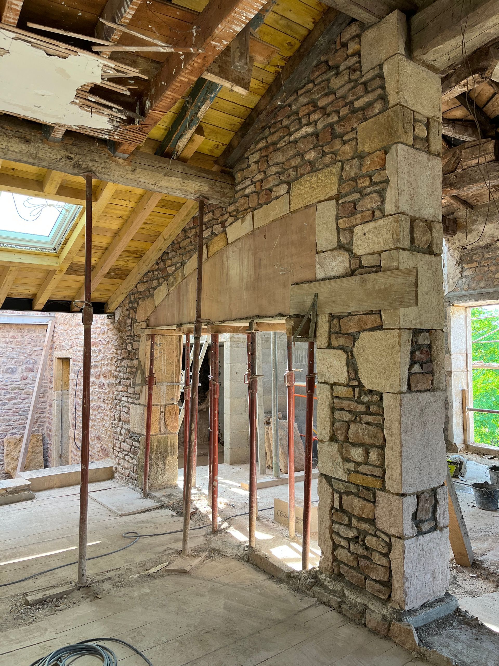 Aménagement intérieur : Murs en pierre, poutres apparentes au plafond, vérins de soutien, plancher en béton.