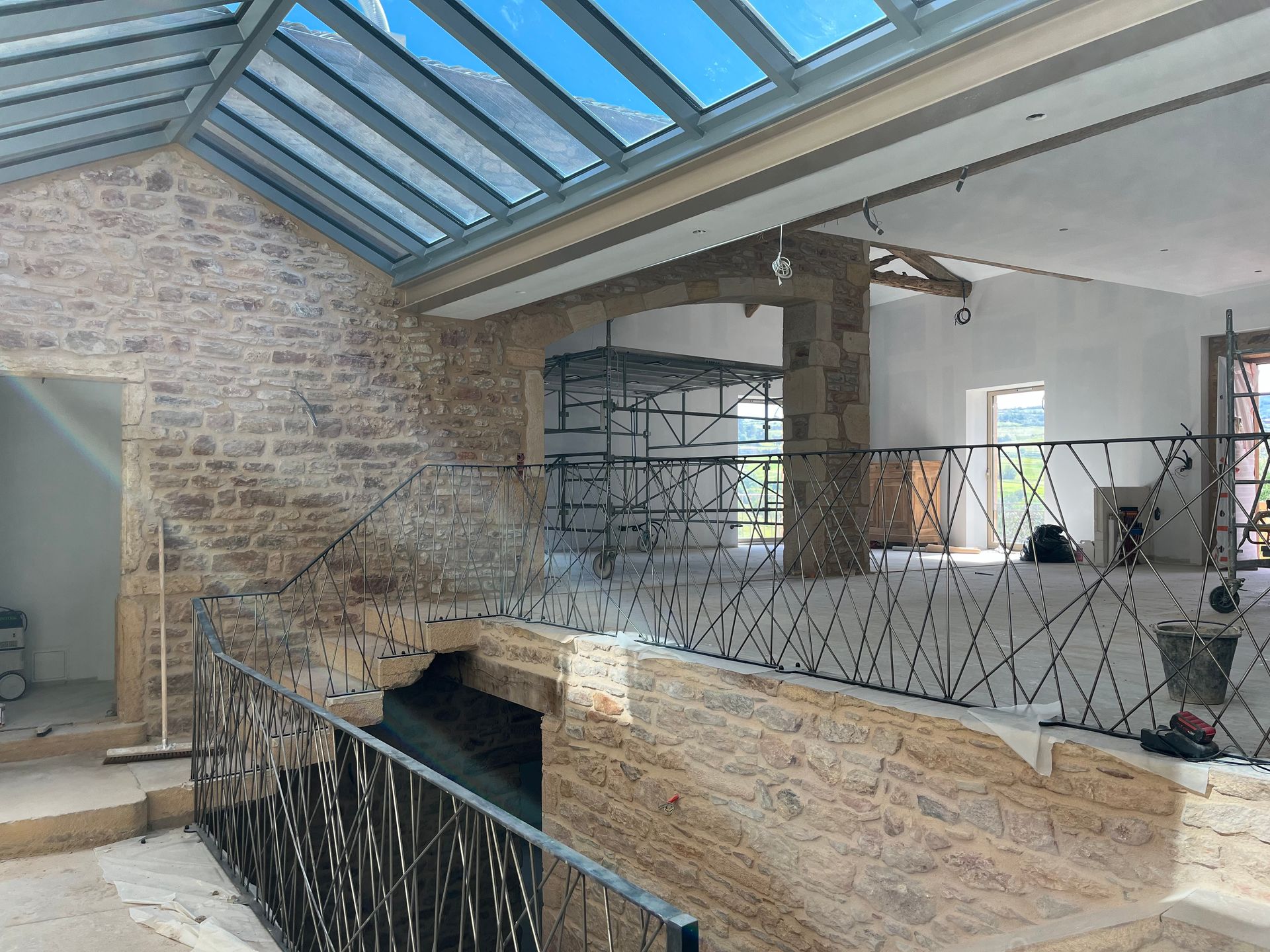 Vue intérieure d'un bâtiment en construction. Murs en pierre, verrière, garde-corps métalliques, échafaudages en arrière-plan.