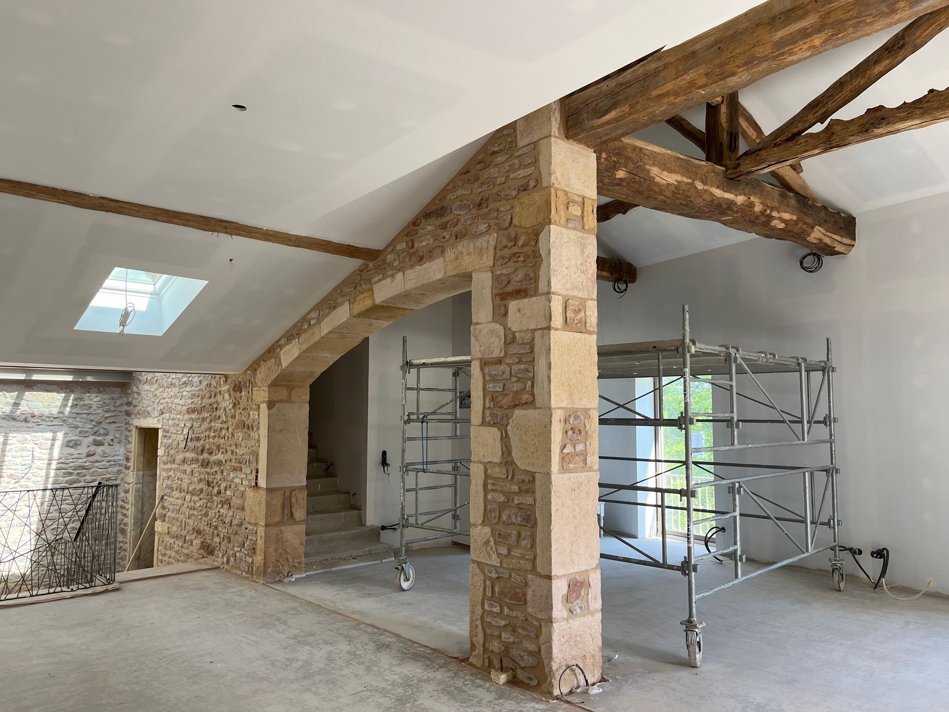 Rénovation intérieure : murs en pierres apparentes et poutres apparentes, échafaudages, luminaires et arcade ouverte.