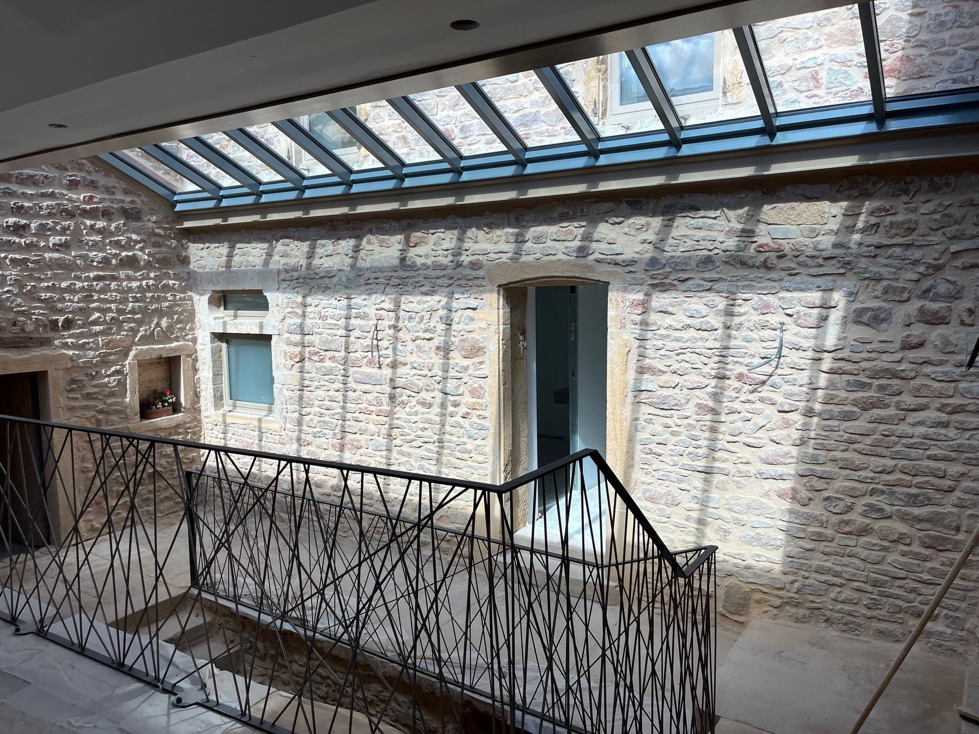 Vue intérieure d'un bâtiment avec des murs en pierre, une lucarne en verre et une balustrade décorative en métal.