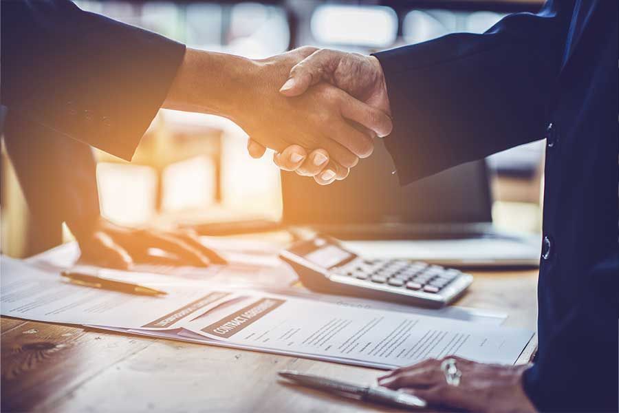 Un avocat serre la main d'un client au-dessus d'un bureau où est posée une calculatrice
