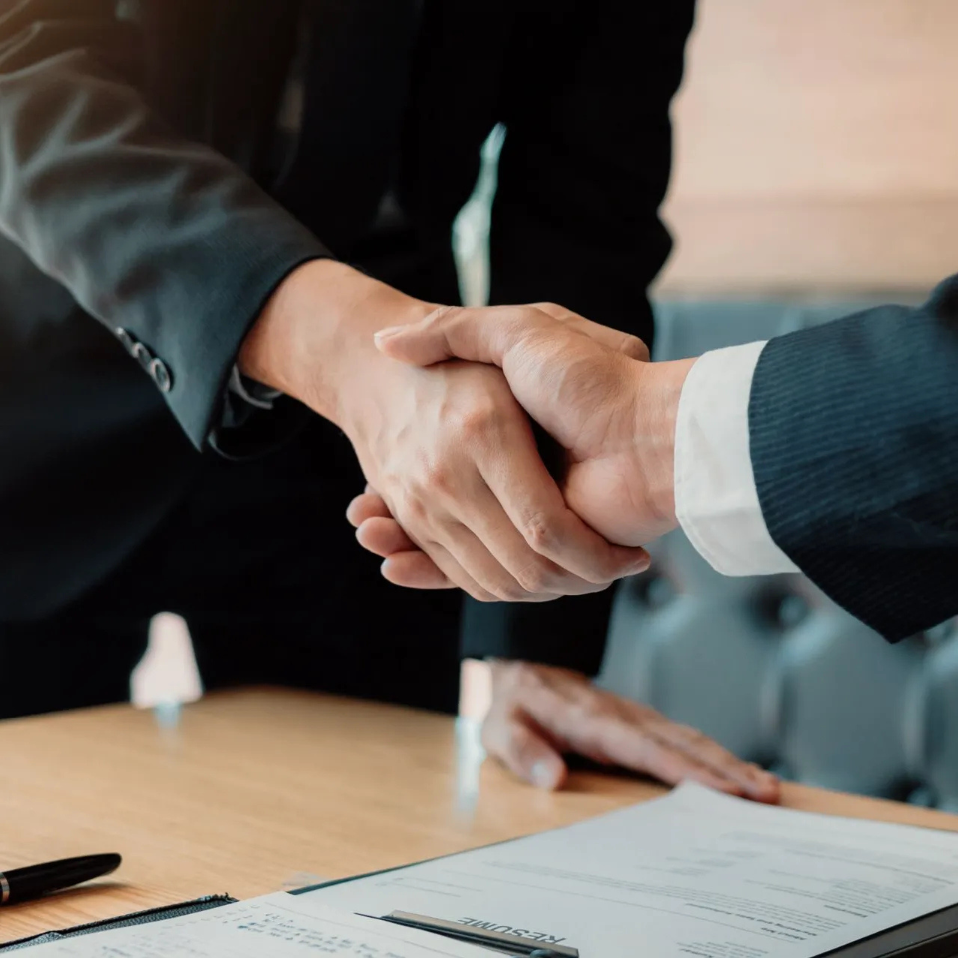 Deux personnes en costume se serrent la main au-dessus d'une table où se trouve un document.
