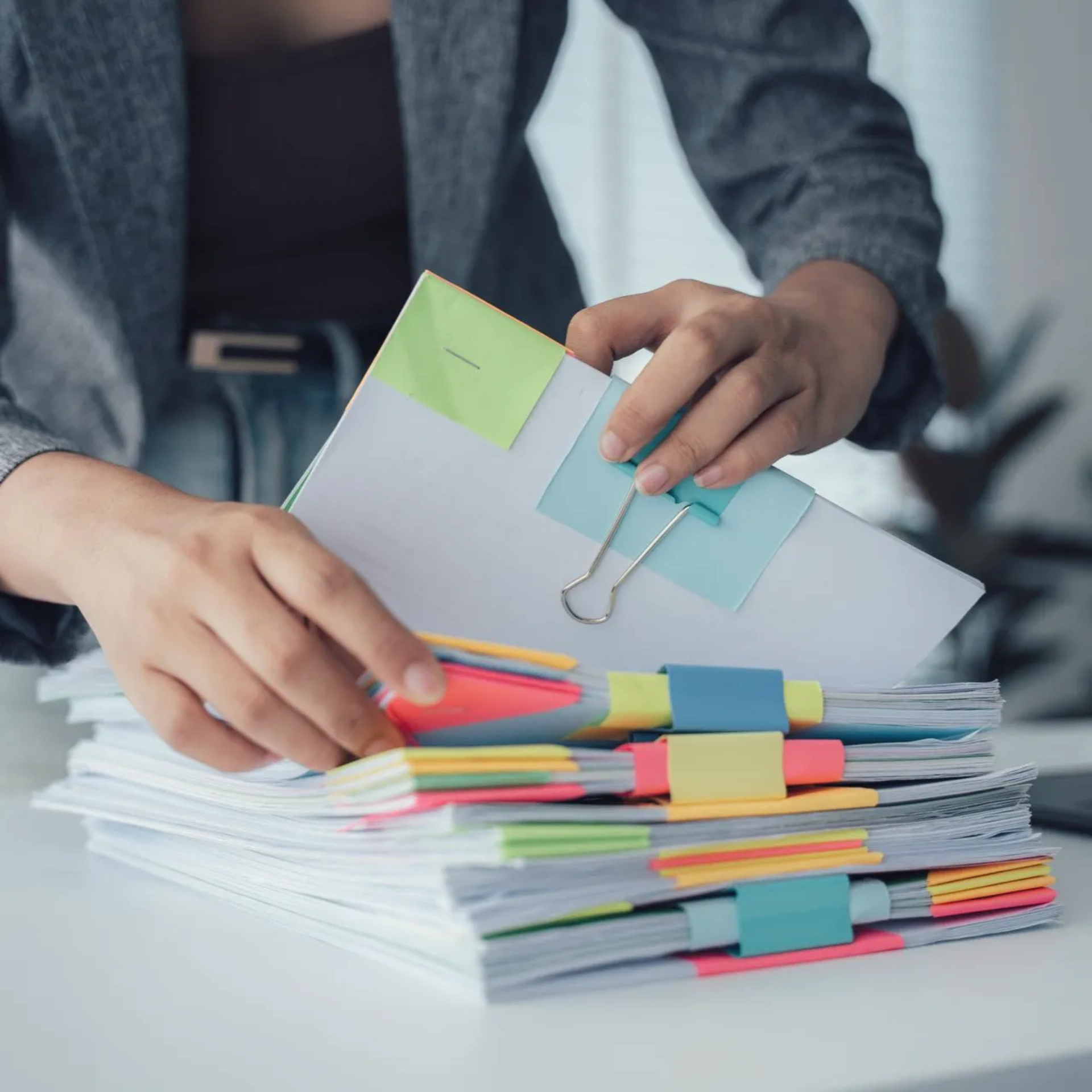 Une personne trie une pile de papiers munis d'onglets colorés et d'une pince à reliure.