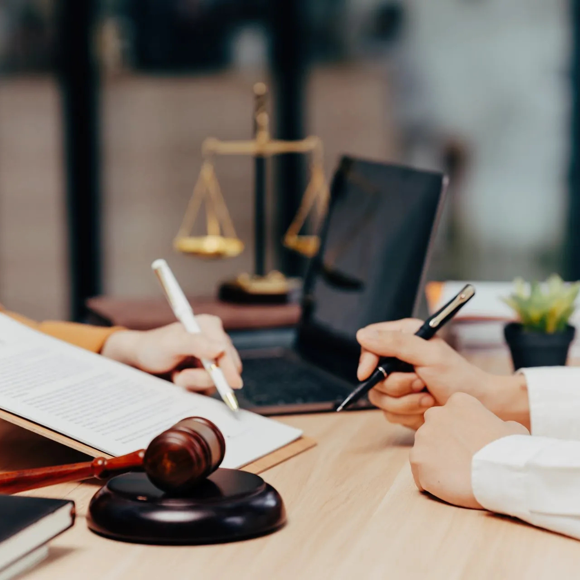 Deux personnes examinent un document sur un bureau où se trouvent un maillet en bois, un ordinateur portable et un symbole de justice en arrière-plan.