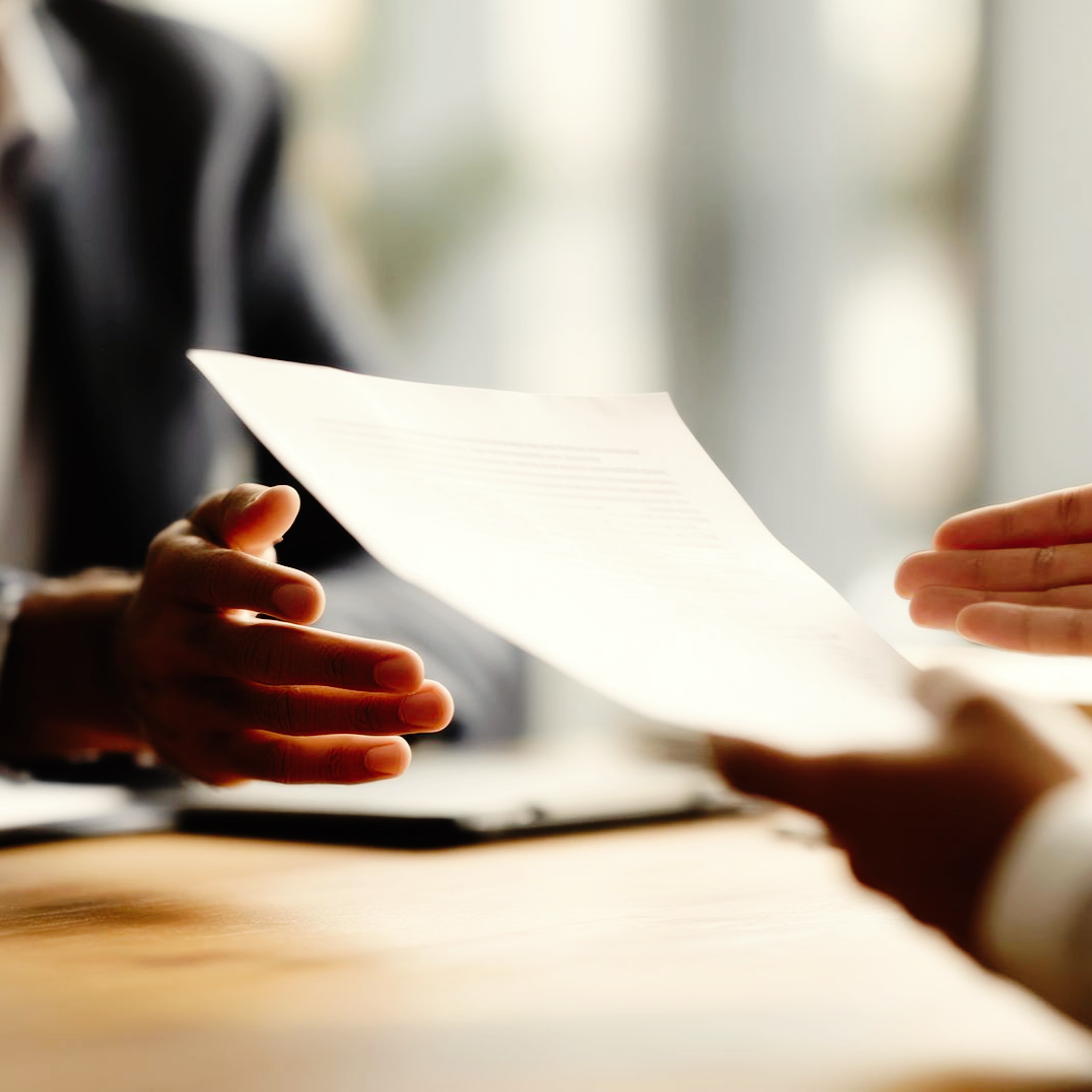 Des mains se passent un document par-dessus une table en bois, dans un bureau.