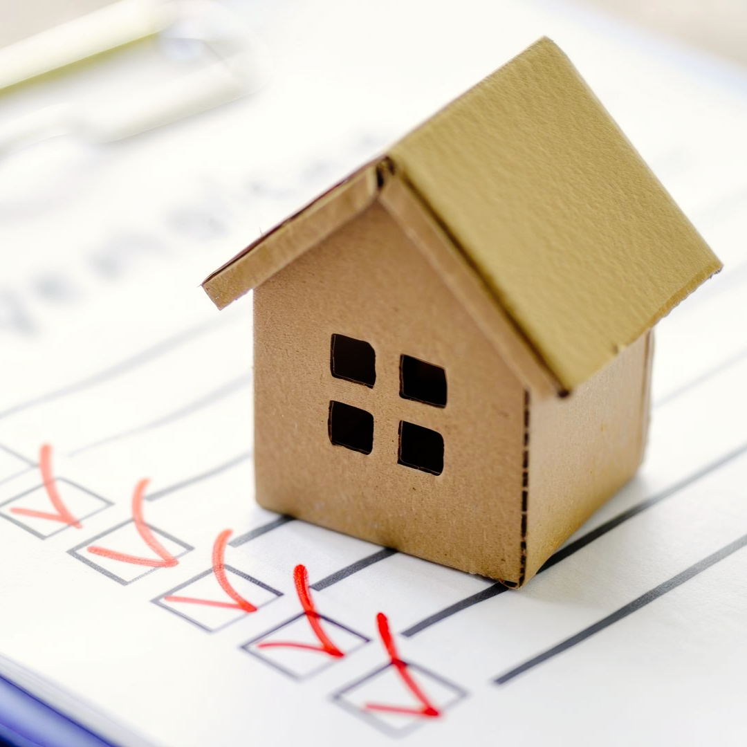 Maison en carton sur une liste de contrôle avec des coches rouges, symbolisant la propriété ou l'inspection du logement.
