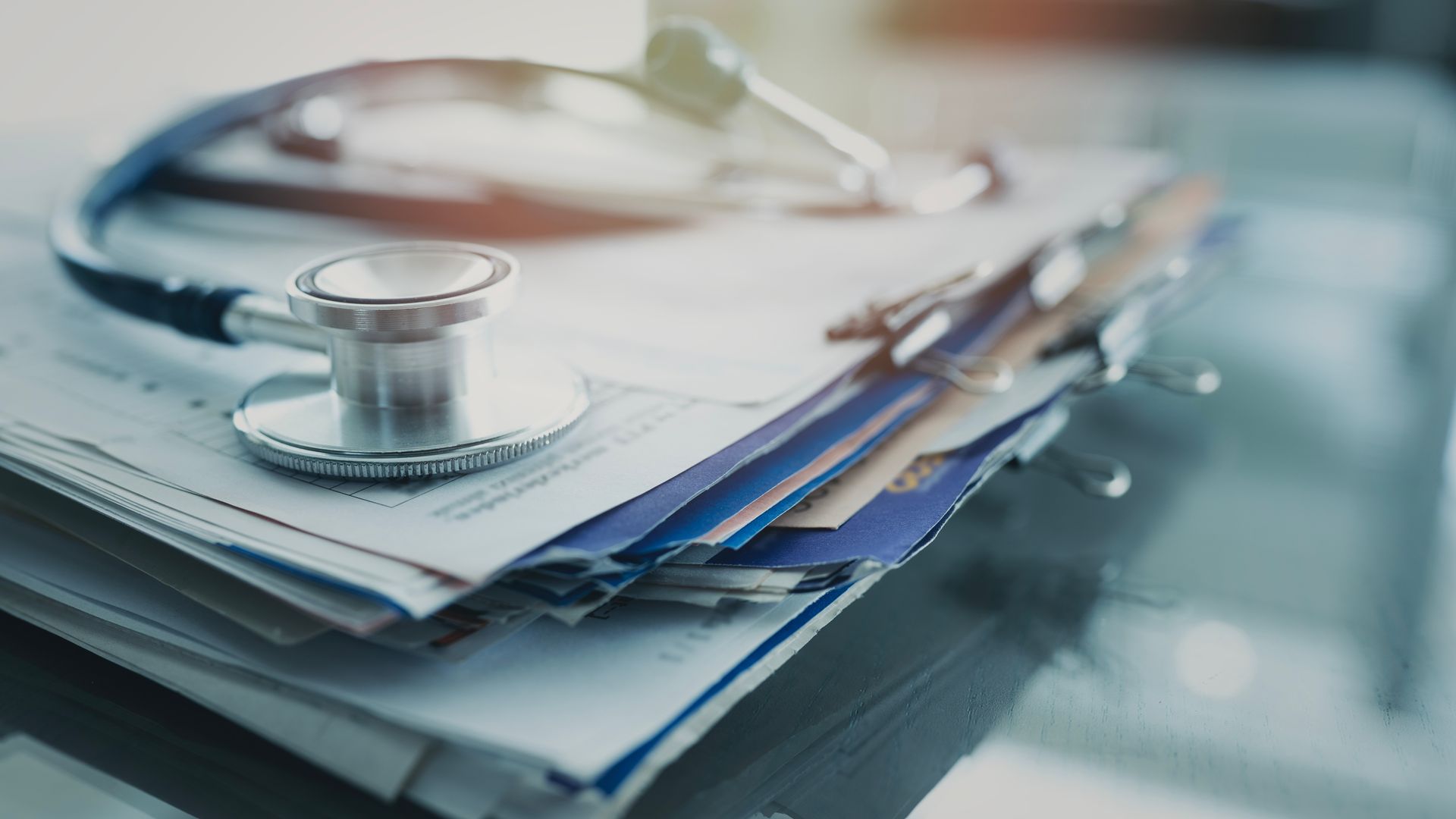 Un stéthoscope médical posé sur une pile de dossiers et de documents de patients, sur un bureau.