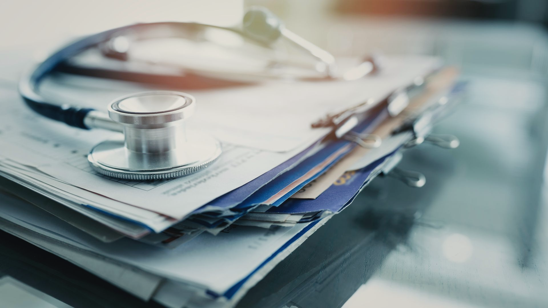 Un stéthoscope en métal posé sur une pile de dossiers médicaux, sur un bureau.