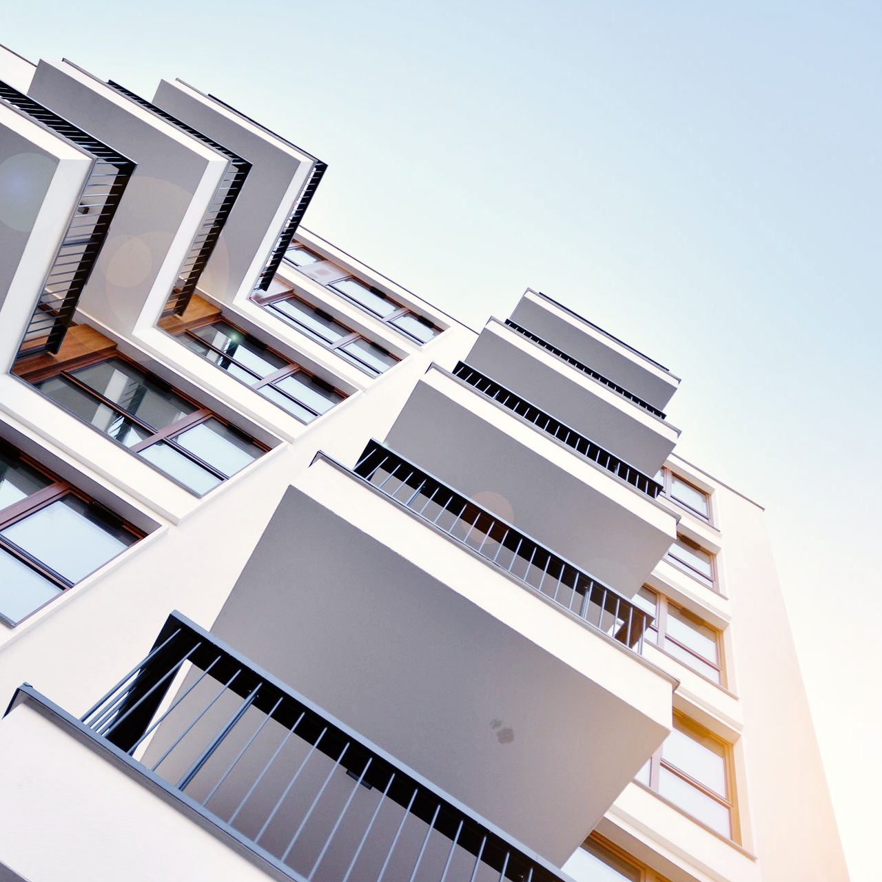 Immeuble d'appartements blanc avec balcons, se détachant sur un ciel bleu, vu d'un angle bas.