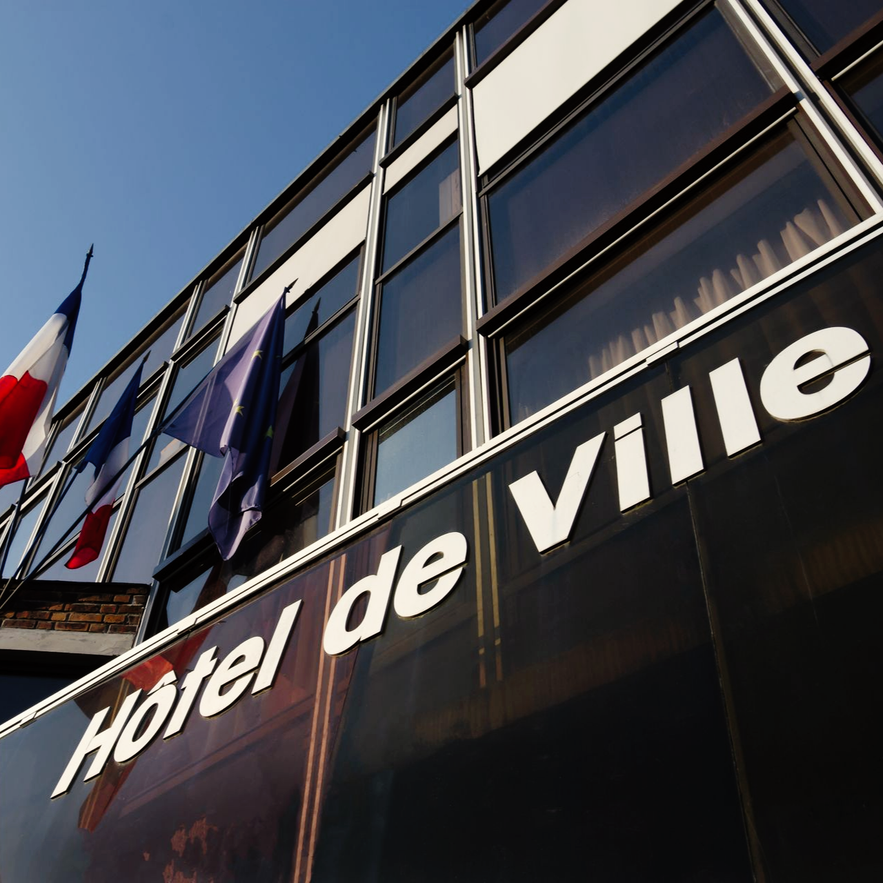 Bâtiment de l'Hôtel de Ville avec des drapeaux français et européens flottant au vent.