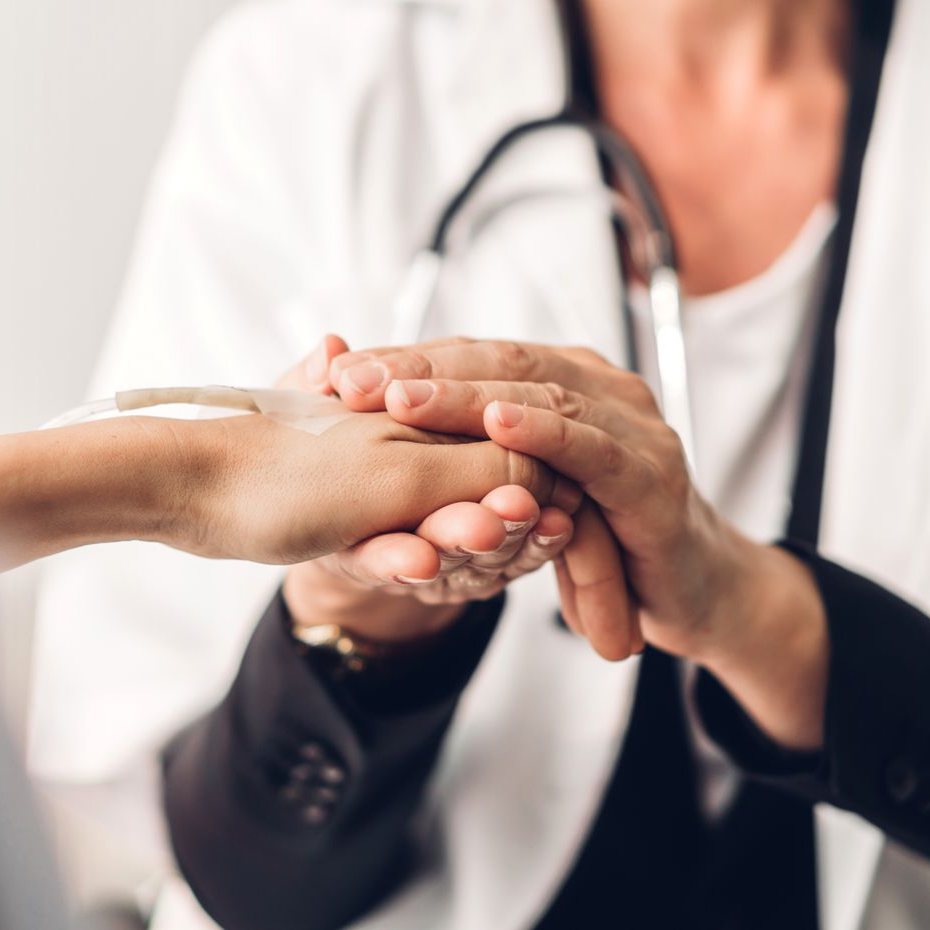 Le médecin tient la main du patient pour le réconforter ; stéthoscope autour du cou, blouse blanche.