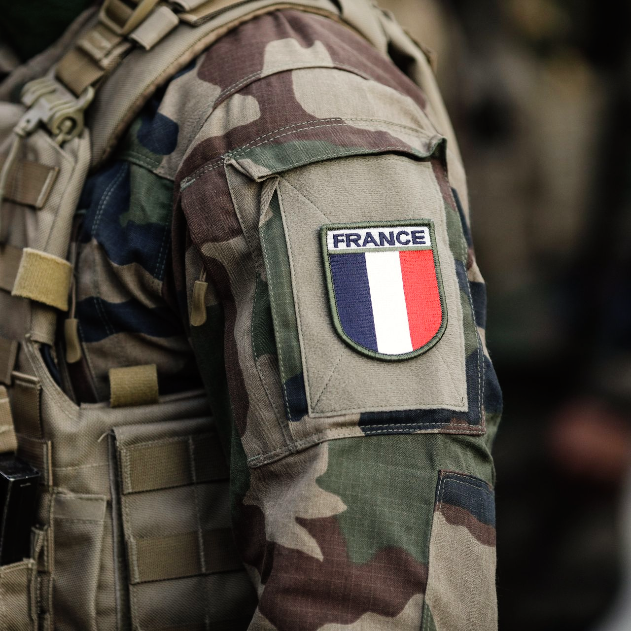 Bras d'un soldat en uniforme de camouflage avec un écusson FRANCE affichant un drapeau bleu, blanc et rouge.