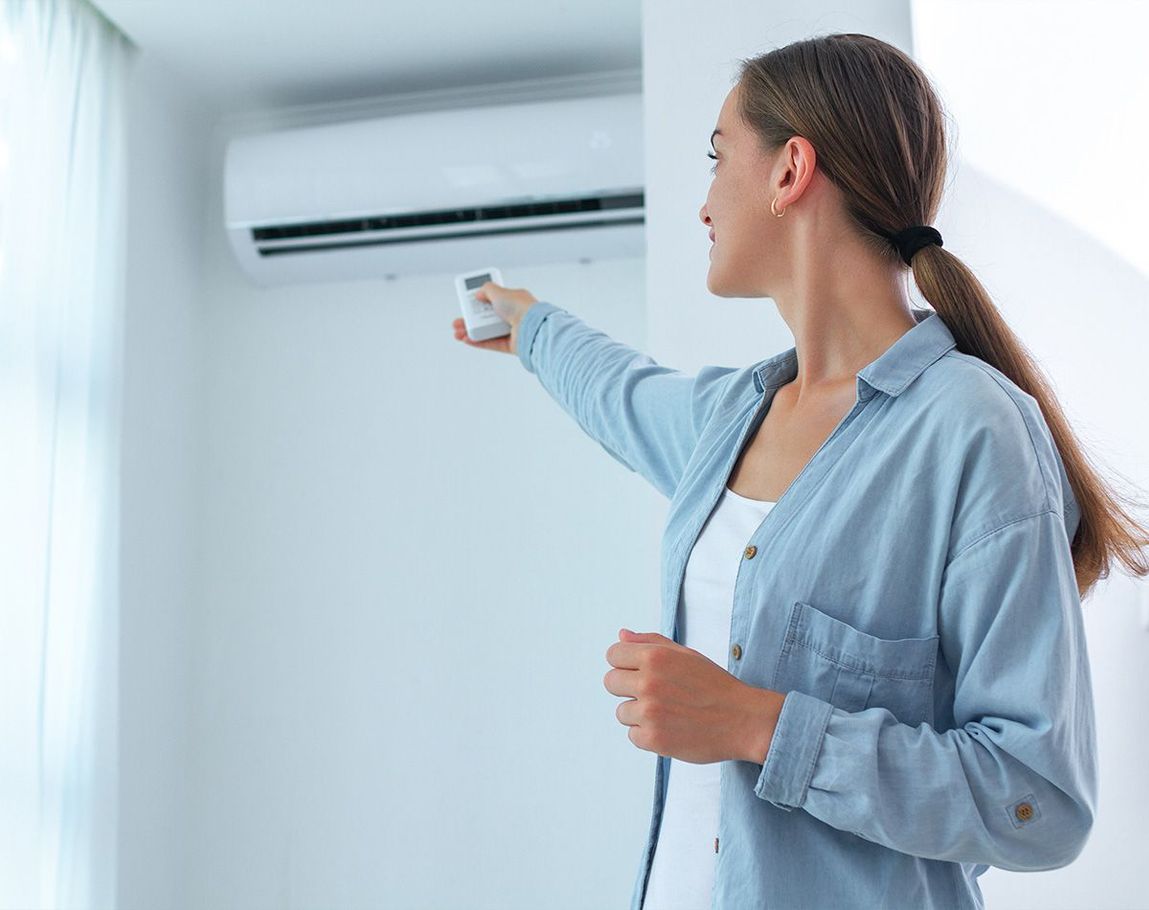 Femme debout tenant une télécommande pointée en direction d'un système de climatisation 