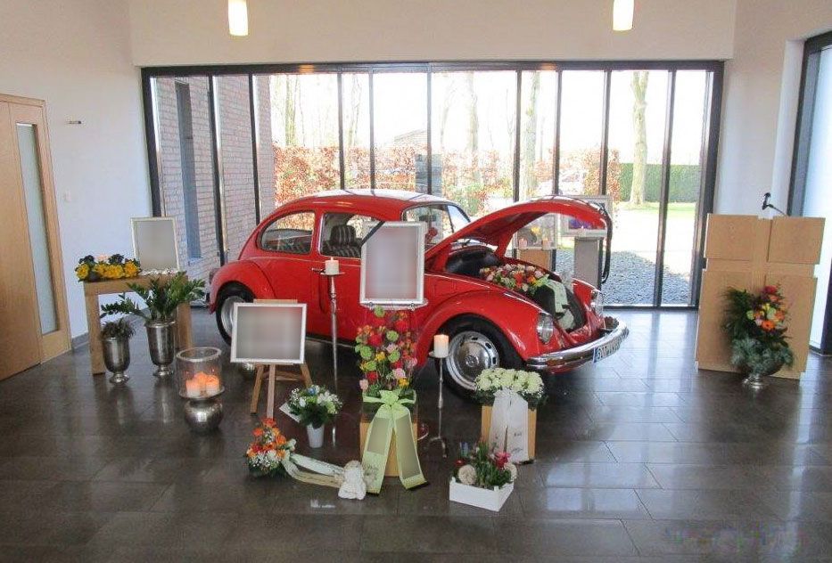 Ein rotes Auto steht in einem Raum mit Blumen und Kerzen - Bestattungen Vornholt in Borken-Burlo