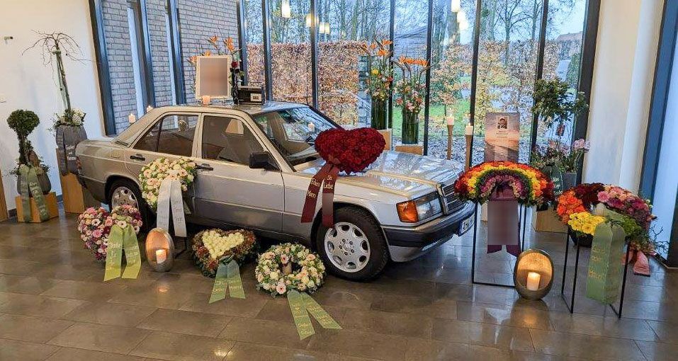 ein weißes Auto, umgeben von Blumen und Kerzen in einem Raum - Bestattungen Vornholt in Borken-Burlo