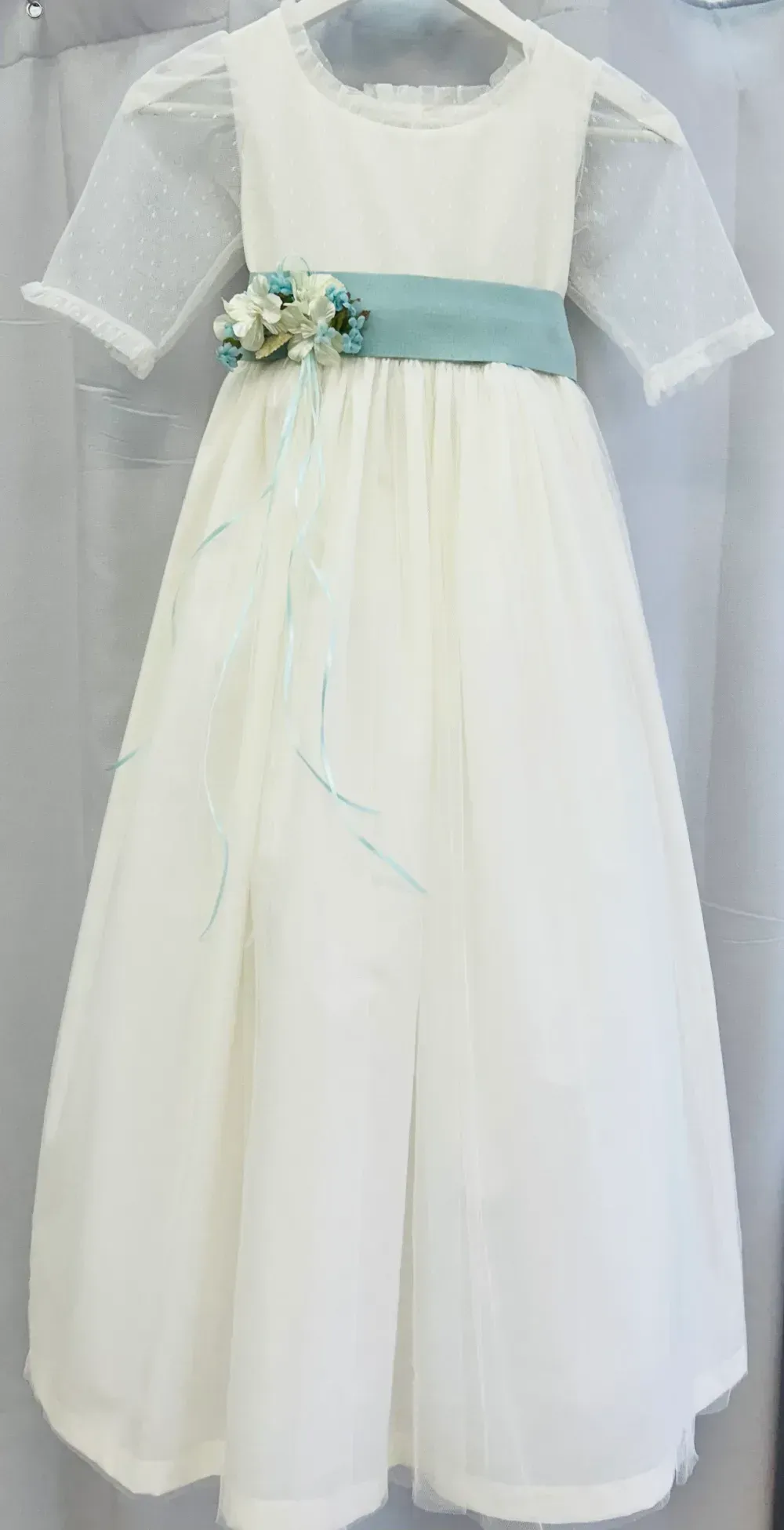 Un vestido blanco con una faja azul cuelga de una percha.
