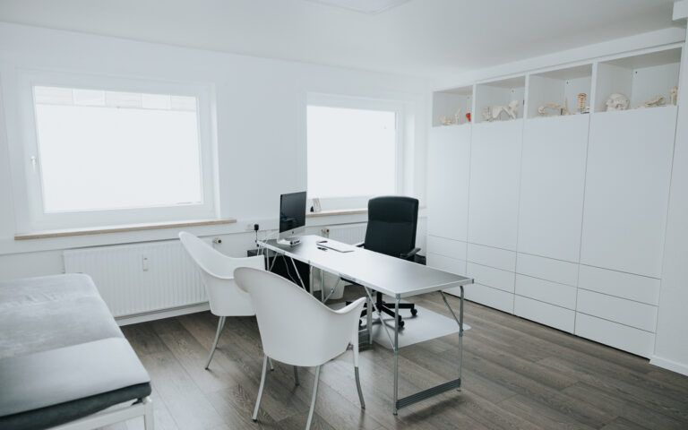 Helles, modernes Heimbüro mit weißem Schreibtisch, schwarzem Stuhl, Sofa und Einbauschränken
