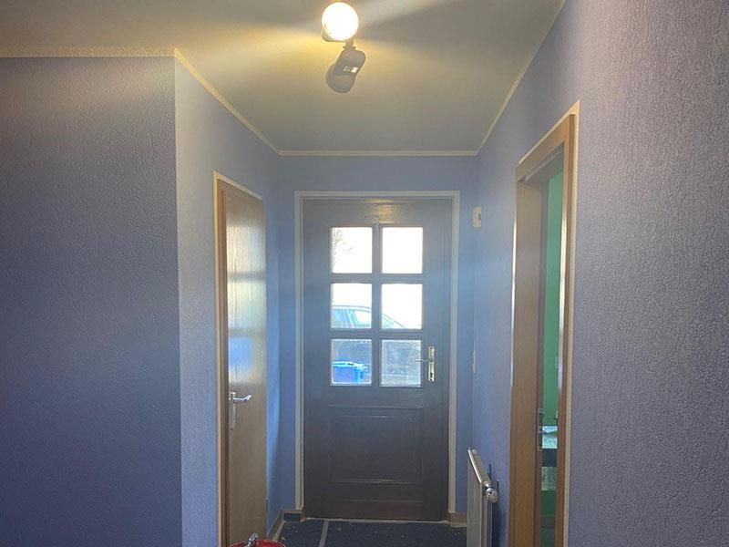 Ein Flur mit violetten Wänden und einer Holztür