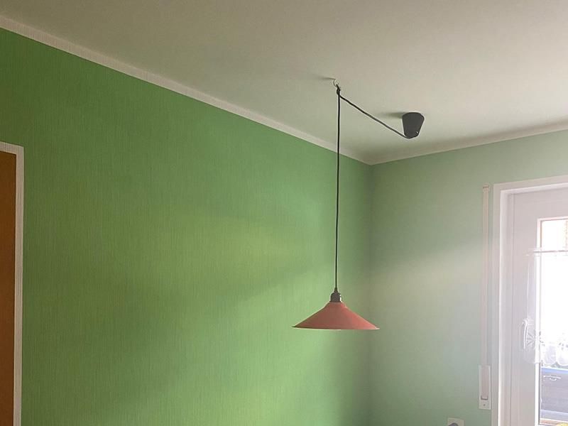 In einem Raum mit grünen Wänden hängt eine Pendelleuchte von der Decke.